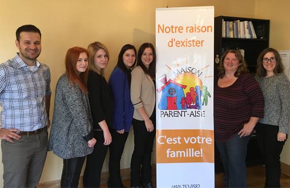 À droite de la bannière, madame Sylvie Côté, coordonnatrice de la Maison Parent-Aise. Cette photo a été prise lors de la conférence de presse annonçant la nouvelle image de l'organisme, organisée par des étudiantes en communication sociale de l'UQTR